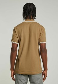 Polo shirt marrone a maniche corte con bordi bianchi sulle maniche e colletto, caratterizzato da un tessuto morbido e un orlo dritto.