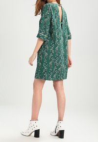 Vestido verde con un patrón floral, mangas cortas y un corte en la espalda. Combinado con botas blancas hasta el tobillo con acentos de tachuelas.
