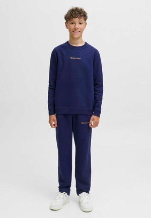 Mörkblå sweatshirt och byxor i en mjuk tyg, med ribbade muddar och en broderad logotyp i guld på bröstet och låret.