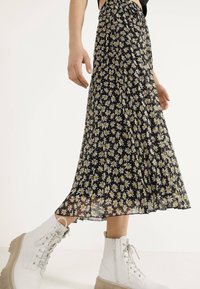 Falda negra con estampado de margaritas blancas y amarillas, ligera, con diseño de tablas, combinada con botas blancas con cordones y suela transparente.