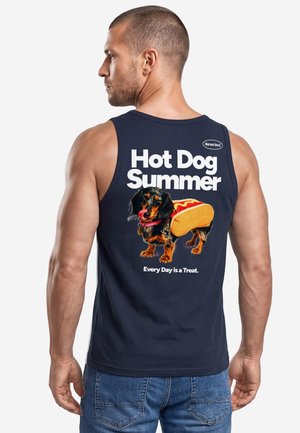 Mann trägt ein marineblaues Tanktop mit dem Text "Hot Dog Summer" und einen Hund, der als Hotdog mit "Every Day is a Treat" auf dem Rücken verkleidet ist.