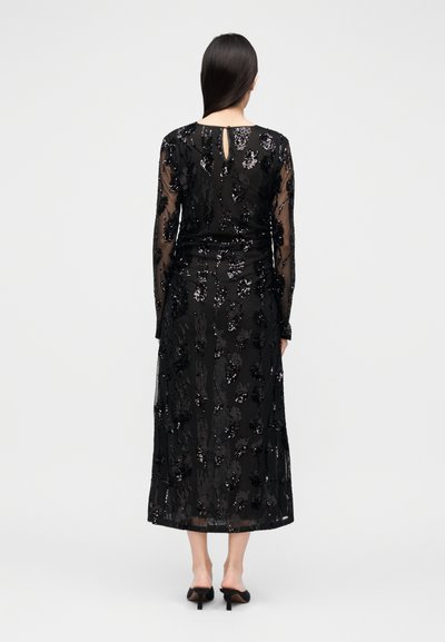 Must pikk kleit pikkade läbipaistvate varrukatega, tikandiga lillemustrite ja litritega. Omab avausega seljaosa ja keha järgivat siluetti.