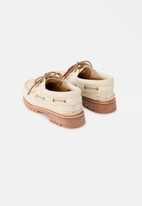 Μπεζ δερμάτινα παπούτσια τύπου boat με καφέ κορδόνια και χοντρές λαστιχένιες σόλες, φωτογραφημένα από πίσω σε λευκό φόντο.