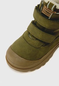 Grüne Wildleder-Winterstiefel mit brauner Gummisohle, zwei Klettverschlüssen und an der Oberseite sichtbarem Fleece-Futter.