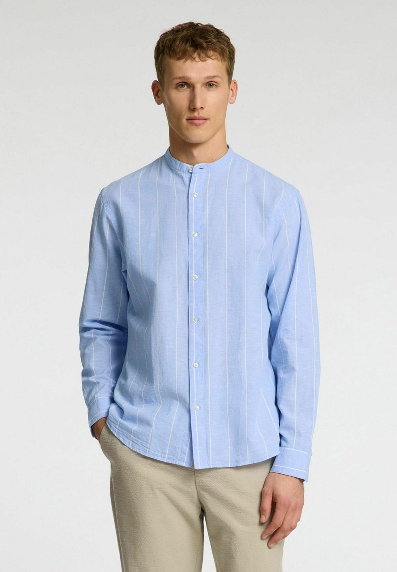 Camisa de manga larga azul claro con rayas verticales blancas, cuello tipo banda y cierre frontal con botones, combinada con pantalones beige. Textura suave.