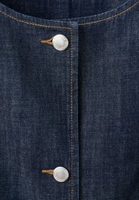 Close-up of dark blue denim fabric with two silver buttons fastened by brown thread and visible tan stitching along the edges.