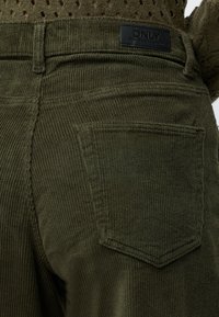 Κοντινή λήψη στην πίσω τσέπη και τη μέση ελαφρώς πρασινωπών βελούδινων παντελονιών με μαύρη ετικέτα που αναγράφει ONLY πάνω από την τσέπη.
