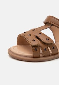 Braune synthetische Sandalen für Kleinkinder mit Stern-Ausschnitten und Akzenten, einem Knöchelriemen, einer flachen Sohle und einer genähten Kante.