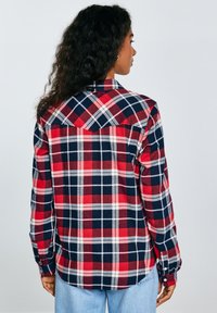 Red and navy plaid flannel shirt with a button-down collar and long sleeves. Features a yoke design and button cuffs. Light fabric texture.