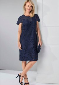 Marineblauw kantjurk met korte kapmouwen, met bloemen uitsnijdingen. Een paar zwarte sandalen met banden en een bijpassende clutch.