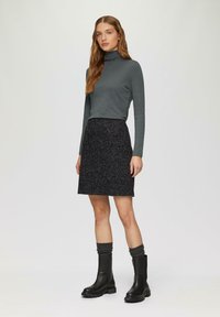 Pull à col roulé gris à manches longues associé à une jupe noire à motifs et des bottes noires à genoux avec des semelles épaisses et des accents de chaussettes côtelées.