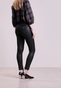 Svarta fusk läder skinnybyxor med en rutigt blus. Outfiten kompletteras av svarta klackar med metalliska klackar.