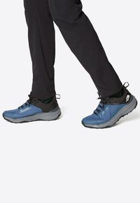 Zapatos de senderismo azules con un acabado texturizado, una sección superior negra y suelas grises. Incluyen cordones y acentos con logo.