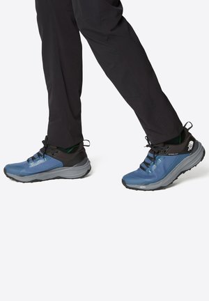 Zapatos de senderismo azules con un acabado texturizado, una sección superior negra y suelas grises. Incluyen cordones y acentos con logo.