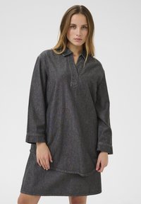 Denim kjole i mørkegrå med lange ærmer, en krave og en løs pasform. Har synlige syninger og en let buet kant.