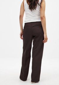 Pantalons marron ajustés avec une coupe droite, dotés de deux poches arrière et d'une texture lisse. Associés à un débardeur blanc côtelé.