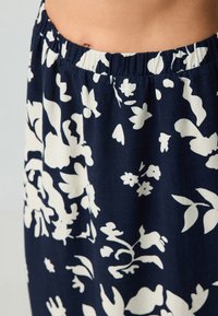Floralprintrock mit elastischem Bund. Mit weißen Blumenmotiven auf einem dunkelblauen Hintergrund. Leichtes Material, die Stoffstruktur ist sichtbar.