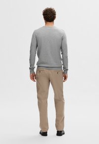 Pull gris pour homme à manches longues, avec poignets côtelés et encolure arrondie, assorti à un pantalon beige et des chaussures noires.