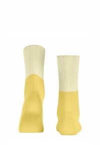 Gelbe und cremefarbene gerippte Socken mit einem Farbblockdesign. Die Oberteile sind cremefarben und gehen am Knöchel in Gelb über. Weiche Textur.