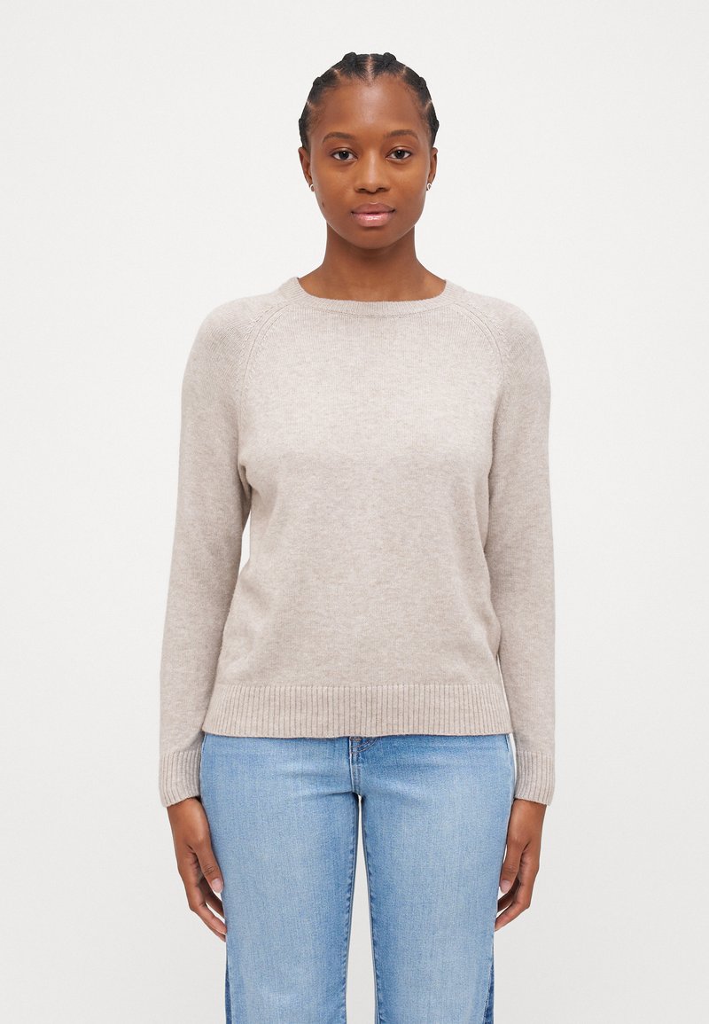Pull en maille beige avec un col rond, ourlet et poignets côtelés, doté de manches raglan et d'une texture douce, associé à un jean en denim.