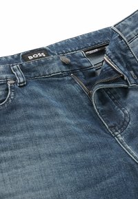 Donkerblauwe denim jeans met een gestructureerde afwerking, voorzien van een metalen knoopsluiting en een ritssluiting aan de voorkant. BOSS-logo op de tailleband.