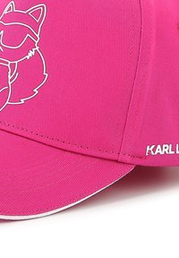 Casquette de baseball rose avec un design de raton laveur en cartoon à contour blanc, en tissu texturé et une accentuation blanche le long de la visière courbée.