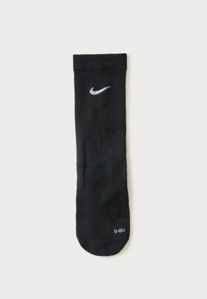 Pojedyncza czarna sportowa skarpeta Nike z białym logo Swoosh w pobliżu mankietu, oznaczona "MD-R" w obszarze palców, położona na płasko na białym tle.