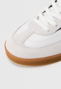 Szary zamszowy sneaker z białym teksturowanym panelem, białymi sznurówkami oraz gumową podeszwą o gładkim wykończeniu i subtelnych detalach przeszycia.