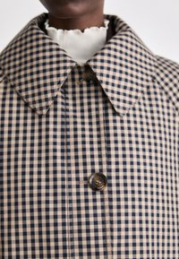 Beige and navy gingham check coat with a wide collar, featuring a single button closure and visible stitching details.