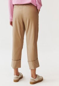 Beige cropped broeken met een gladde textuur, met opgerolde zoom en een hoge taille. Gepaarde met lichte schoenen en een roze trui.