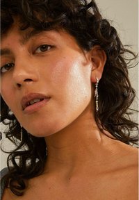 Pendientes de gota de plata con acentos texturizados y pequeños detalles de perlas, presentados en un modelo con cabello rizado y tono de piel natural.