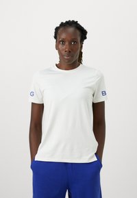 Valge lühikeste varrukatega T-särk ümmarguse kaelusega ja sinise logo detailiga vasakul varrukal. Sile tekstuur, mugav lõige.