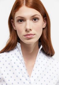 White shirt with a blue floral pattern, standing collar, and smooth texture. Close-up view of a model's face and neckline.