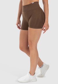 Bruine sportshorts met een hoge tailleband, een gladde textuur en een getailleerd ontwerp, gecombineerd met witte ademende sneakers.