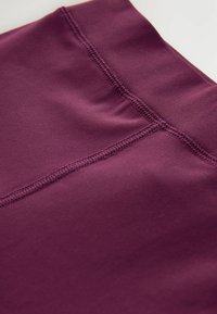 Leggings de sport bourgogne avec une texture lisse, des coutures à plat et une large taille pour plus de confort.