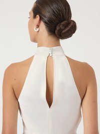 Λευκό φόρεμα με λαιμόκοψη halter και κλειστό πίσω μέρος, που διαθέτει κουμπί κλειδώματος και λείο satina υφή. Ασημένια στρογγυλά σκουλαρίκια συμπληρώνουν την εμφάνιση.