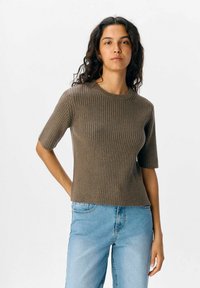 Top corto a maniche corte a coste marrone con scollatura a girocollo; abbinato a jeans azzurri. Design semplice, vestibilità comoda e superficie testurizzata.