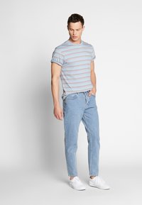 T-shirt a righe di colore blu chiaro con maniche arrotolate, abbinato a jeans blu chiaro e sneaker bianche. L'outfit presenta un design casual e dal taglio rilassato.