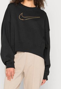 Black cropped sweatshirt made of soft fabric with a gold dotted Nike logo across the chest. Features wide sleeves and a relaxed fit.