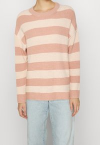 Pull rayé rose et crème avec une texture côtelée et un col rond. Associé à un jean bleu clair, ample.