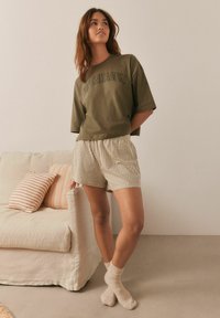 Olive green oversized t-shirt with "Copenhagen" print, paired with beige checkered shorts. Worn with light brown ribbed socks.