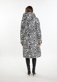 Přestřihnutý kabát s pruhy zebra v černé a bílé barvě, se stahovací kapucí a páskem v pase, dlouhými rukávy a délkou do poloviny lýtek.