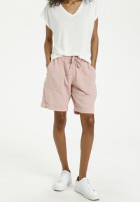 Pantaloni corti rosa chiaro con una vestibilità rilassata, vita elastica e cordoncino, dotati di due tasche laterali. Abbinati a una t-shirt bianca con scollatura a V.
