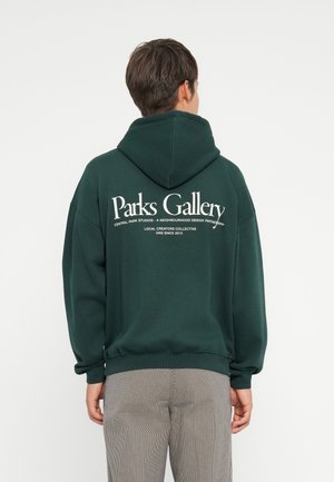 Groene hoodie met een groot wit logo-tekst op de achterkant, voorzien van een trekkoord capuchon en geribde manchetten, gemaakt van zachte stof.