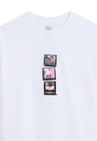 Drie gestapelde vintage televisies met kleurrijke statische beelden en vervormde afbeeldingen op een witte Vans t-shirt.