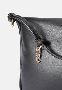 Mustakos leather-käsilaukku, jossa on sileä pinta, kaareva muoto ja kultainen "Furla" -merkki yksityiskohtana hihnassa.