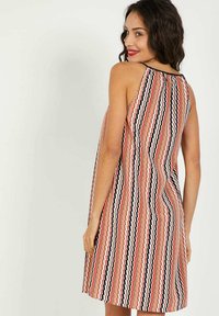 Un vestido sin mangas, de largo hasta la rodilla, que presenta un patrón geométrico en tonos rojos, negros y crema, con un detalle de espalda fruncida y una tela ligera.