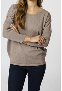 Beige oversized sweater with ribbed sleeves and a round neckline, worn with dark blue jeans, featuring a relaxed fit and soft texture.