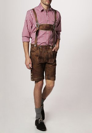 Ruskeat nahkaiset lederhosenit säädettävillä remmeillä ja napin koristeilla, yhdistettynä puna-valkoiseen ruudulliseen paitaan ja harmaisiin polvipituihin sukkiin.