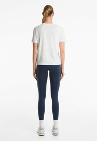 Top bianco a maniche corte e leggings navy, con una vestibilità slim. I leggings sono abbinati a calze bianche e scarpe da ginnastica.